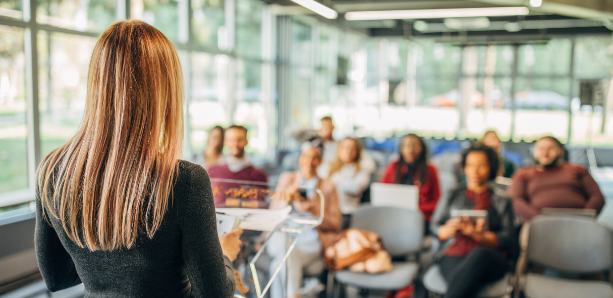 Woman giving a presentation to an engaged audience in a modern, well-lit conference room.