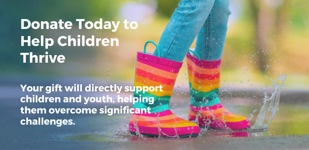 Child wearing colorful rainbow-striped rain boots splashing in a puddle.